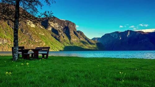 Timelapse: Beauty of Norway with mountain range, lake water, green grass, blue sky and bench under t