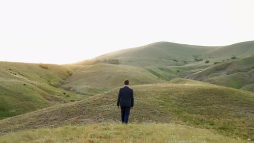 A Man in a Suit Walks Through the Hills Towards the Sunlight Spring Green Mountain Landscape