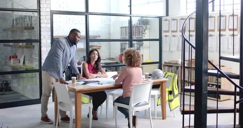 Diverse male and female architects having meeting and looking at blueprints at office, slow motion