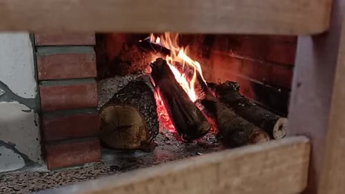 Lebendige Flammen und brennende Baumstämme in einem gemauerten Kamin, umrahmt von einem Holzstuhl