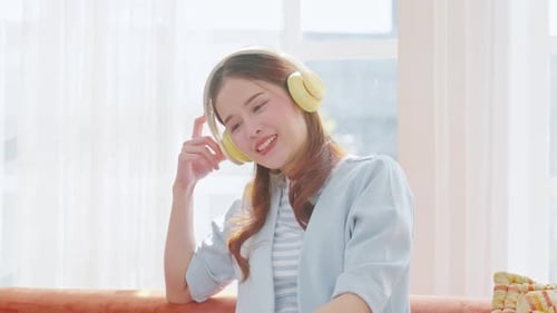 Happy Asian young woman wear headphone listen and enjoy with music at home. Attractive female close