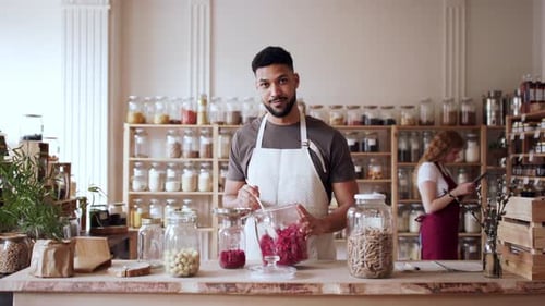 Young Man Filling Jar by Dryed Raspberries in Zero Waste Shop, Looking