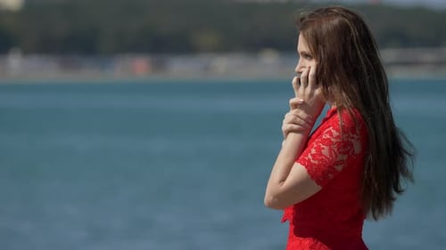 Woman dressed in red talking by the phone near sea