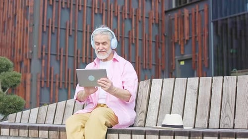 Old Man with Headphones Engrossed in Tablet on Wooden Bench