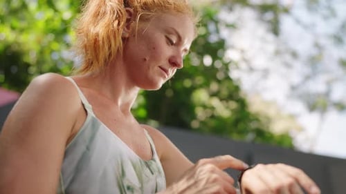 Redhead Woman Athlete in Tropical Gym Checks Fitness Tracker on Smart Watch Female Adjusts Settings