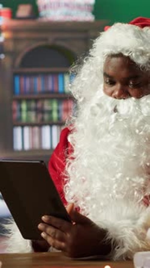Vertical Video Santa Claus Uses a Tablet to Navigate Online Webpages in His North Pole Cabin