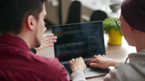 Two Hipster Coworkers Sharing Ideas About Project Sitting with Laptops in Spacious Open Space Office