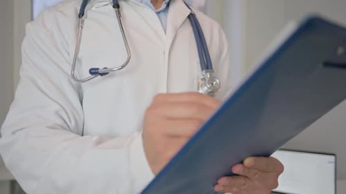 Doctor Taking Notes on Clipboard in Exam Room
