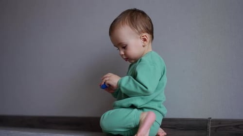 Tiny Caucasian boy in green sport suit plays on the floor of the room.