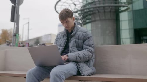 Male Student Studying on Campus Using a Laptop with Books Nearby