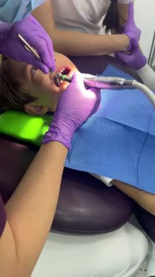 A Doctor Dentist in a Medical Mask and Purple Rubber Gloves Puts a Seal on a Little Boy Toddler