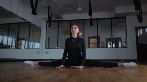 Realización de una elegante pose dividida en un estudio de baile bien equipado para practicar