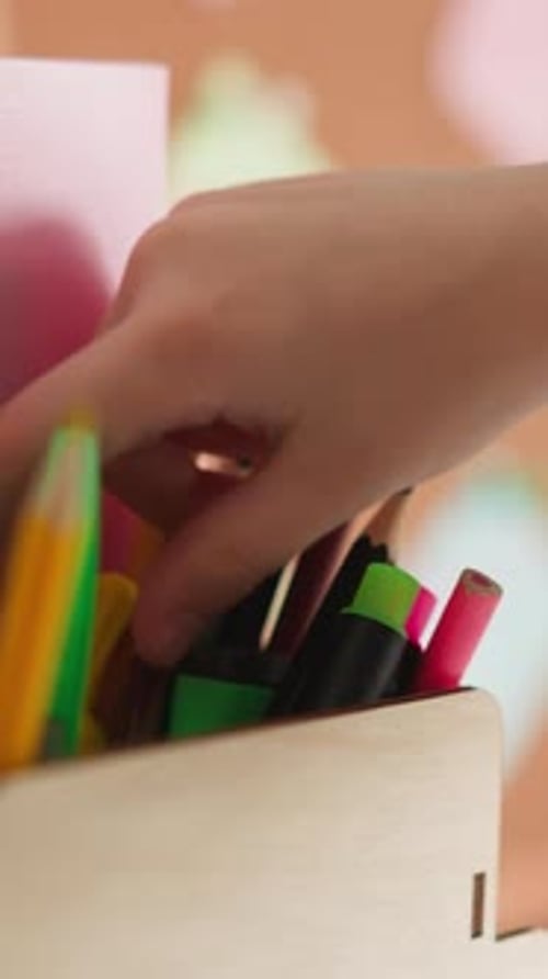 Girl Chooses Pencil for Drawing in Wooden Holder on Table