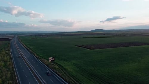 Road with Cars and Trucks on It Passes Through Fields Under a Colored Sky