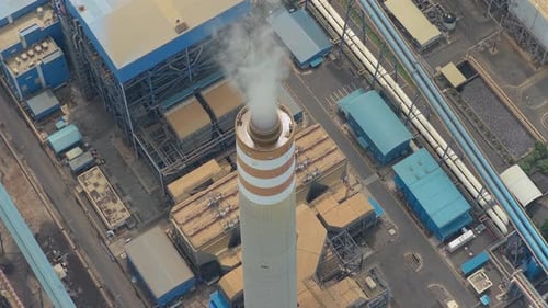 High aerial perspective of a coal fired power plant with a tall smokestack emitting plumes of