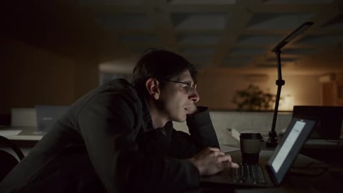 Junger Mann liest Text auf dem Laptop, als er nachts Überstunden im Büro macht