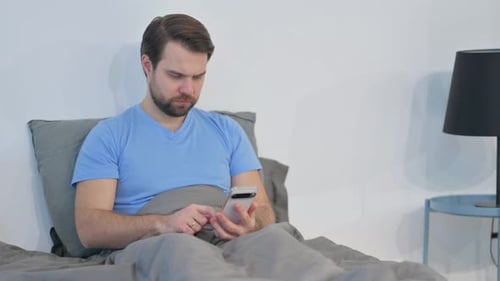 Man Using Smartphone While Relaxing in Bed