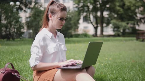 Woman Working on Laptop Outdoors in Urban Park Setting During Sunny Afternoon Enjoying Nature While