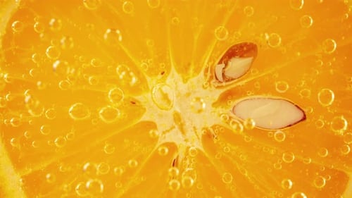 Eine Scheibe reifer Orange im Wasser sprudelt auf einem orangefarbenen Hintergrund.