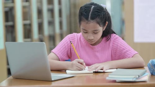 Elementary school girl is doing homework and learning online at library in school.
