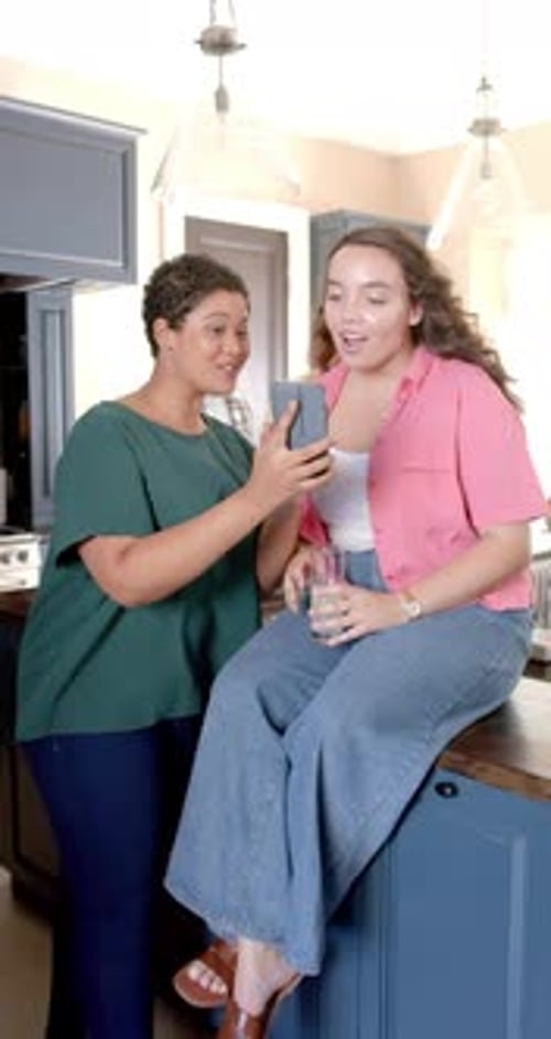 Vídeo vertical: mostrando el smartphone a una amiga, mujeres sonriendo y disfrutando del tiempo en la cocina