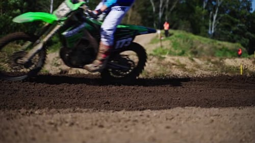 Motocross racer passing by on motorcycle splashing mud riding bike on dirt track during championship
