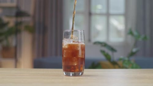 Fresh Cola Being Poured In To The Glass With Ice Cubes On Table