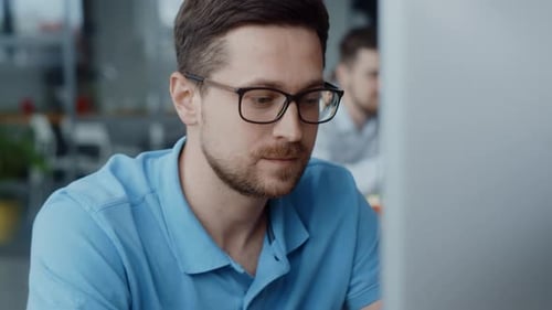 A Focused Man in Glasses Analyzes Information on His Laptop