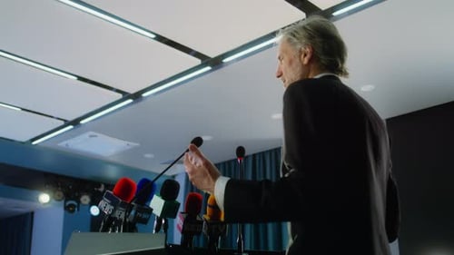 Adult Man Speaks at a Podium with Microphones
