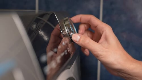 Closeup Hand of Unrecognizable Man Adjusting Washing Machine Settings for Laundry in Cozy Utility