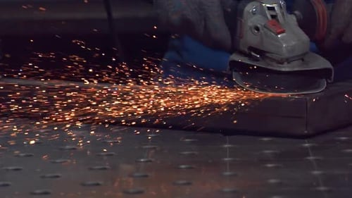 Blacksmith cutting metal using angle grinder while working in industrial workshop. Ultra Slow
