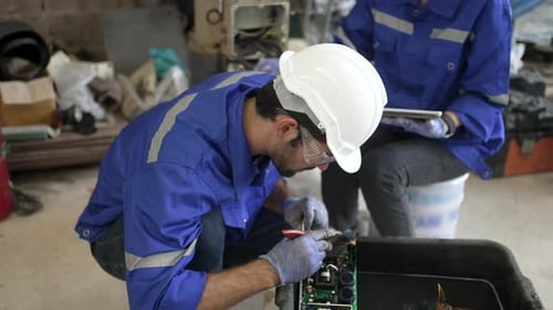 Trabajadores manuales en un taller de máquinas con brazo robótico de soldadura.