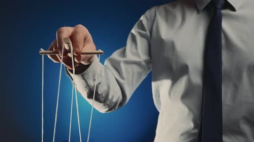 Un hombre de negocios con camisa gris y corbata negra controla una marioneta con un manipulador de madera y cuerdas