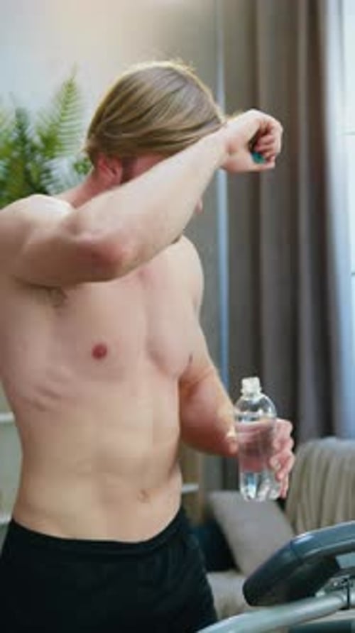 Shirtless Man Hydrating After Exercising on Treadmill