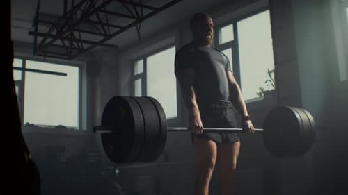 Bearded Sportsman Practices Deadlifts with Barbell in Gym
