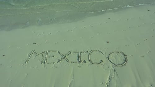 Turning shot of MEXICO inscribed in the sand on a beach.