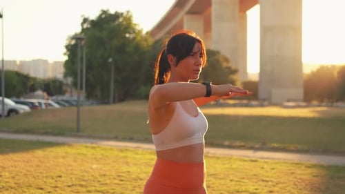 Sporty Woman Stretching Arms at City Park During Bright Sunny Day