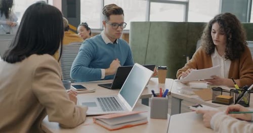 Business Team Discussing Project Pointing at Charts Sitting Around Table in Office