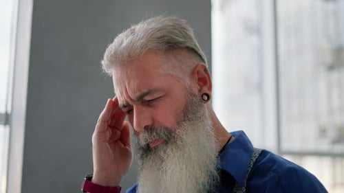 Close Up an Elderly Man with Gray Hair a Lush Beard and a Ring in His Ear in a Blue Shirt Massages
