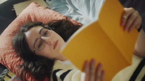 Woman Reads Book Lying on Couch