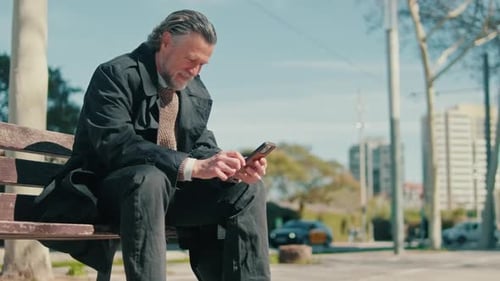 Happy Senior Man Using Smartphone in City Park