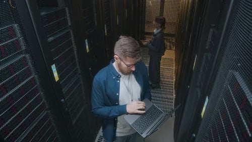 Young IT Technicians Inspecting Rack Server Cabinets in Data Center Together