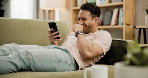 Man Laughing Using Smartphone Lying on Couch Indoors