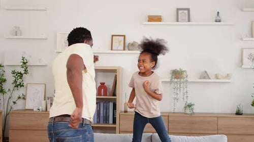 an active father and his little daughter share laughter as they jump and dance on the sofa.