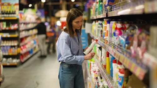 Mujer joven que elige productos de limpieza en el pasillo del supermercado