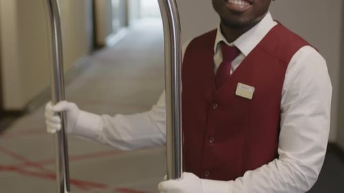 Portrait of Joyous Bellhop with Luggage Cart in Hotel Hallway