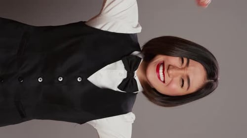 Vídeo vertical: conserje de hotel asiático flexionando los músculos de los brazos en un estudio gris