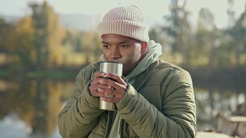 Man Drinking Hot Drink by Calm Lake in Autumn