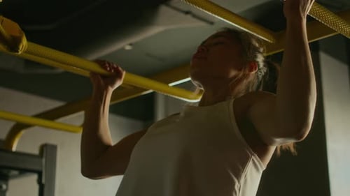 Junge asiatische Kampfkämpferin führt Klimmzüge an Bars im Fitnessstudio durch
