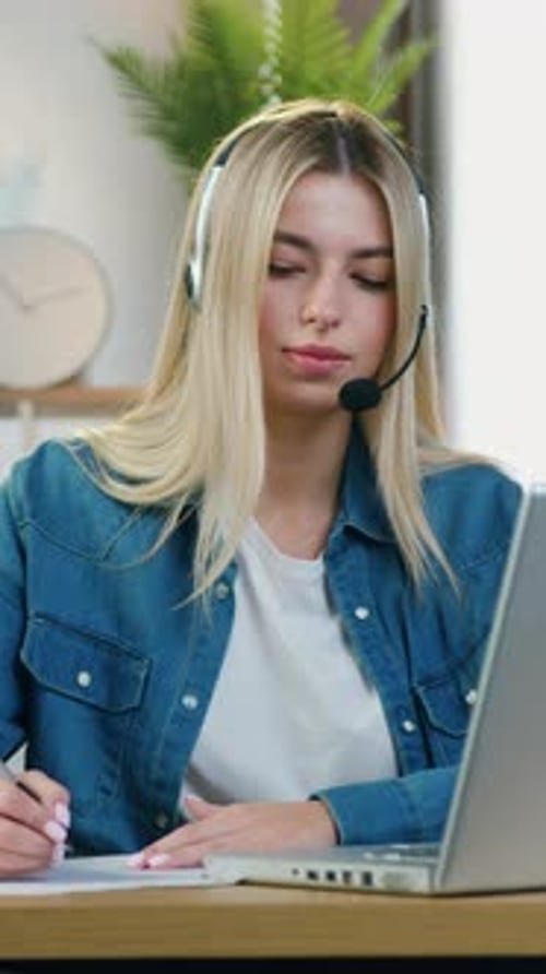 Woman with Headset Taking Notes While Using Laptop